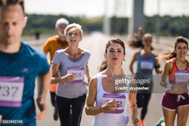 ung bestäms kvinna kör ett maraton lopp med andra konkurrenter på vägen. - halvmaraton bildbanksfoton och bilder