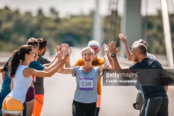 fröhlichen senior läufer gruß ihre anhänger im marathonlauf. - marathon ziel stock-fotos und bilder