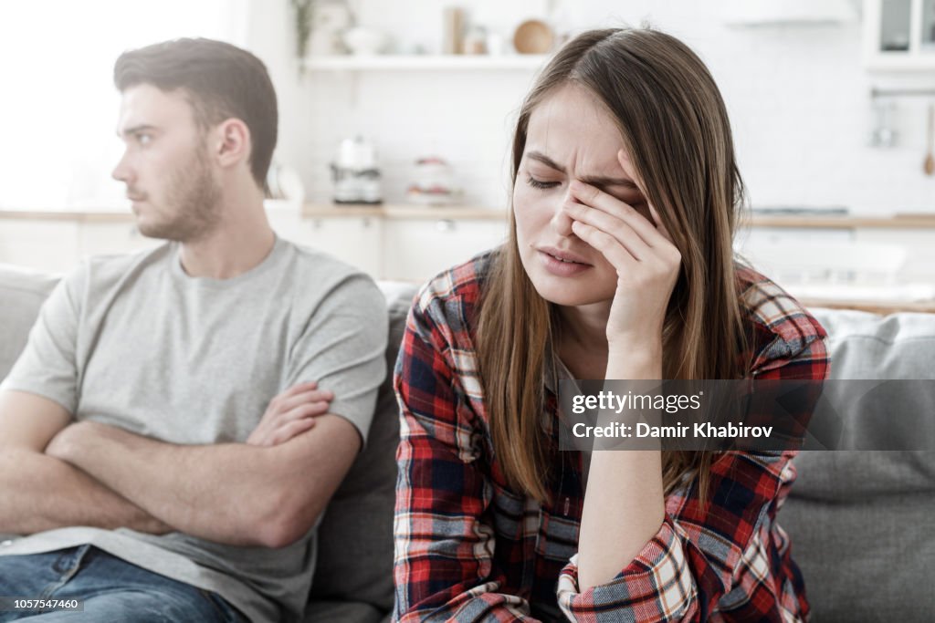 Couple conflict. Stressed crying female sitting on couch with abusive husband after quarrel, ready to divorce