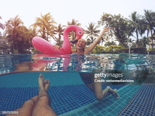 underwater point of view of young couple having fun in resort swimming pool with inflatable flamingo with palm trees on background. - pov or personal perspective or immersion stock pictures, royalty-free photos & images