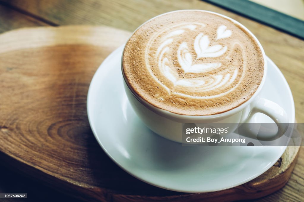 Close-up of a cup of hot latte coffee on the wooden table.