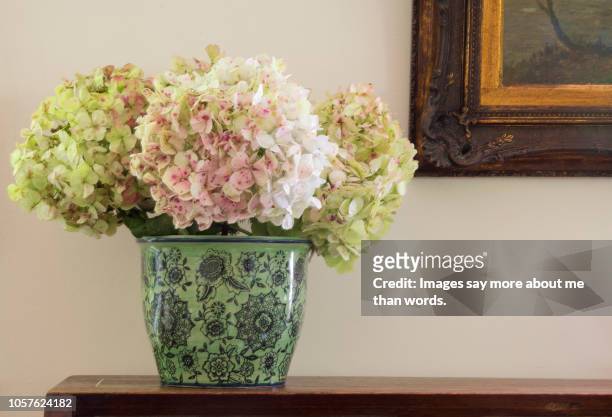 a green vase with some hydrangeas over against a wall and a part of a painting's frame. still life. - flower pot stockfoto's en -beelden