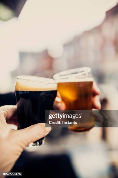 close-up shot of a couple cheering with two different kind of beers, on the patio of a microbrewery - ale stock pictures, royalty-free photos & images