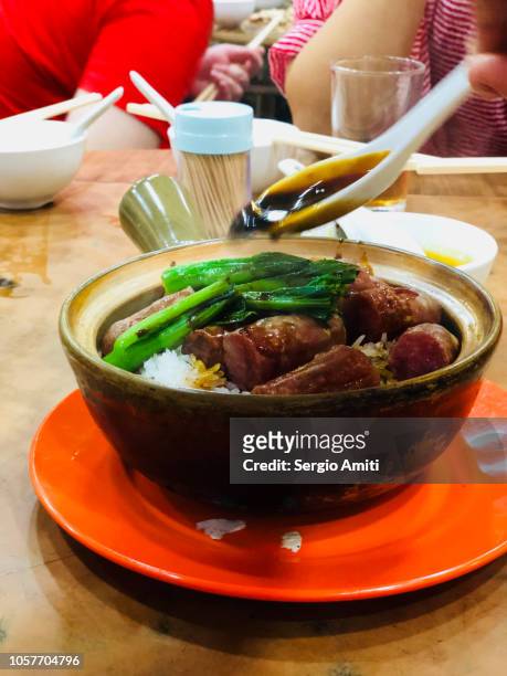 adding oyster sauce to a clay pot rice with chinese sausage using a spoon - panchina stockfoto's en -beelden
