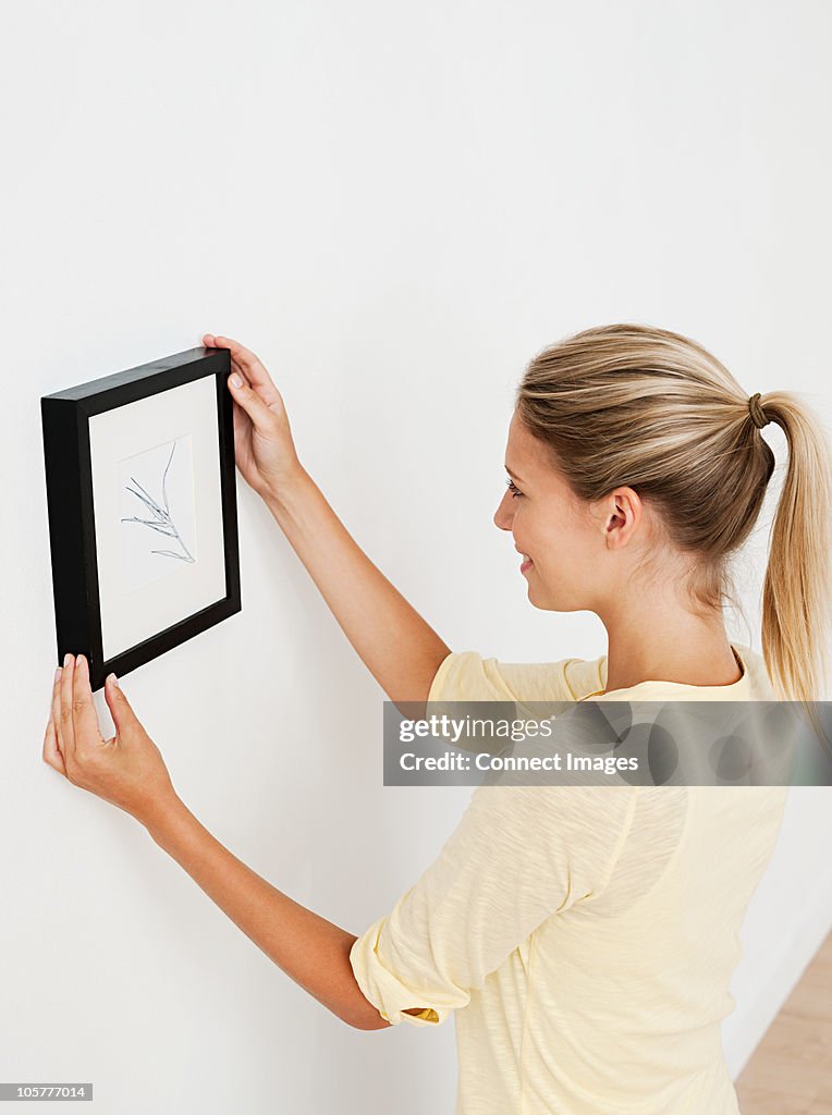 Young woman hanging picture on wall