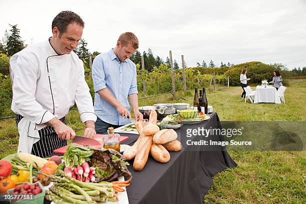 men preparing food for dinner party in field - food industry stock pictures, royalty-free photos & images