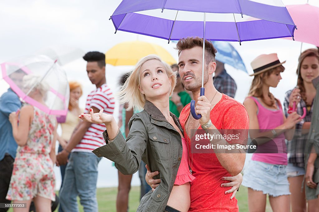 Young couple under umbrella at festival, testing for rain