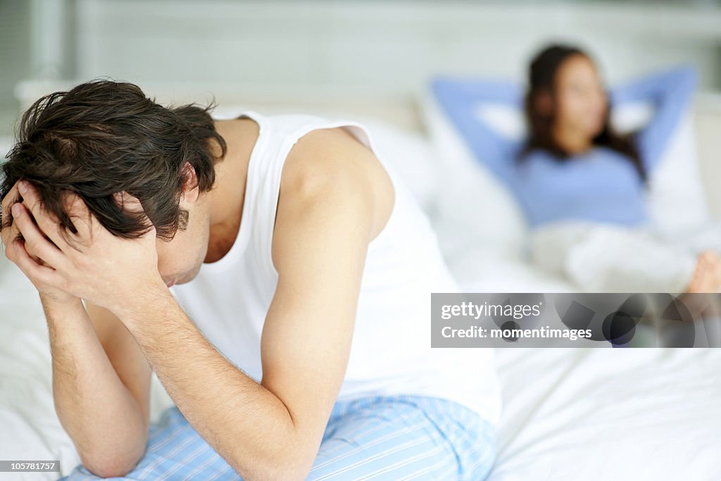 Frustrated man sitting on edge of bed