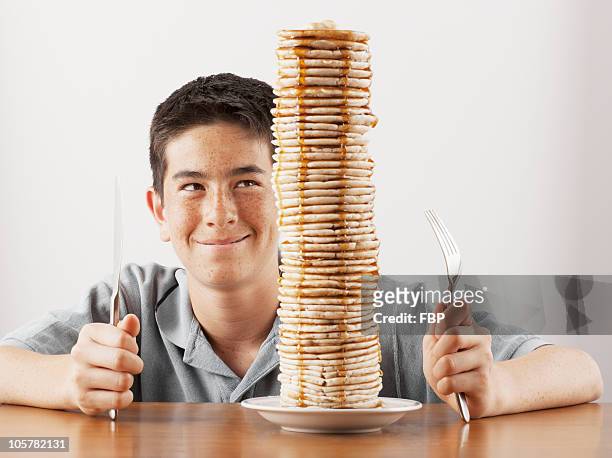 young boy sitting behind a tall stack of pancakes - in tischhöhe stock-fotos und bilder
