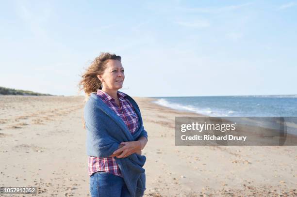 mature woman standing on the beach looking out to sea - shawl stock pictures, royalty-free photos & images