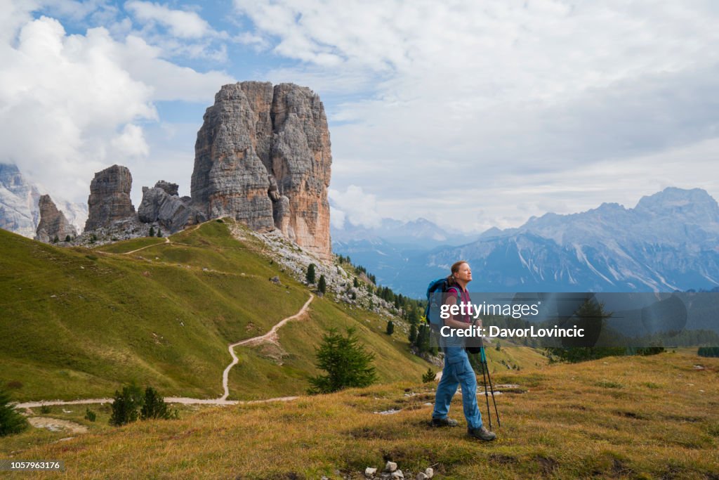 Mujer Senior es senderismo en campo de hierba con rocas de cinco torres (Cinque Torri) en el mítico corazón de los Dolomitas, Italia.