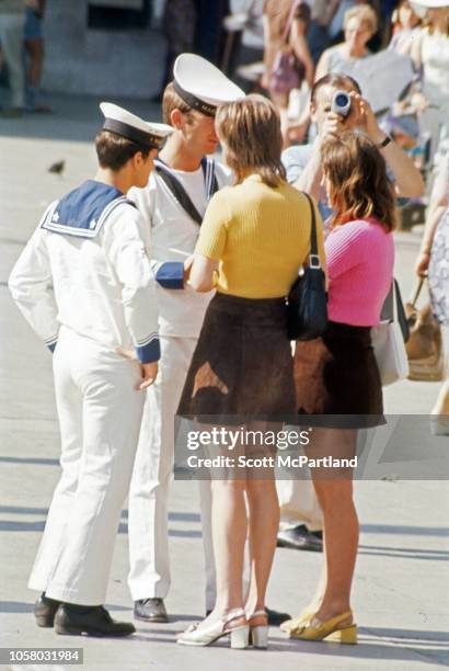 Two uniformed sailors talk with a pair of women, both dressed in bright tops and miniskirts, Siena, Italy, August 1968.
