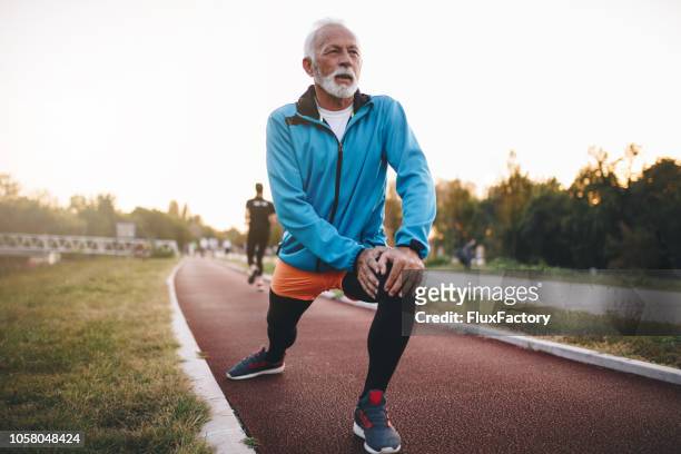 senior man uitrekken tijdens het joggen op een atletiekbaan - warm up exercise stockfoto's en -beelden