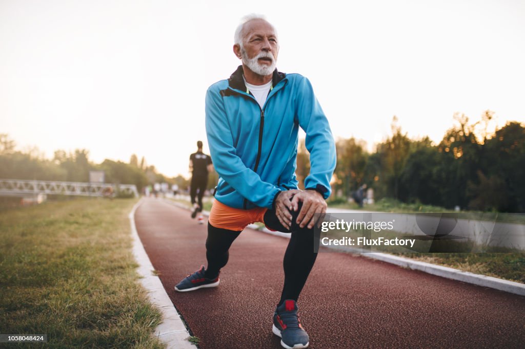 Senior man stretching while jogging on a running track