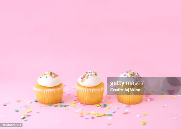 frosted cupcakes with sprinkles on pink background with confetti. - cupcake stock pictures, royalty-free photos & images