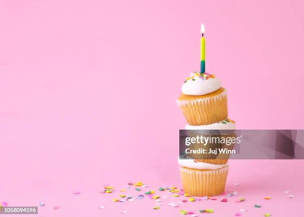 frosted cupcakes with sprinkles and candles on pink background with confetti. - cupcake stock-fotos und bilder