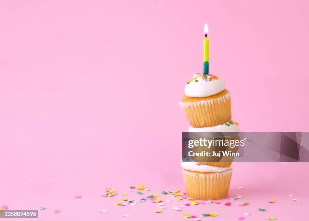 frosted cupcakes with sprinkles and candles on pink background with confetti. - cupcake candle stock pictures, royalty-free photos & images