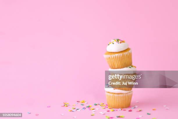 frosted cupcakes with sprinkles and candles on pink background with confetti. - cupcake foto e immagini stock