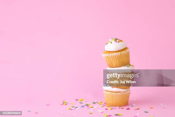 frosted cupcakes with sprinkles and candles on pink background with confetti. - confeito colorido para bolos imagens e fotografias de stock