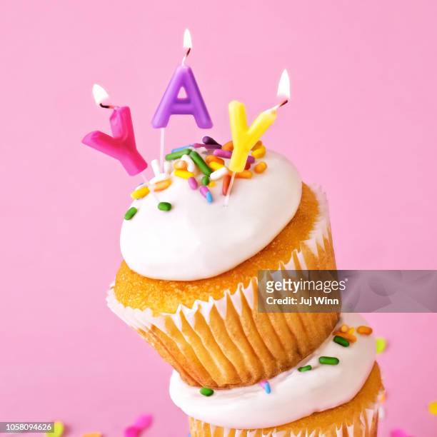 frosted cupcakes with sprinkles and candles on pink background with confetti. - indulgence stockfoto's en -beelden