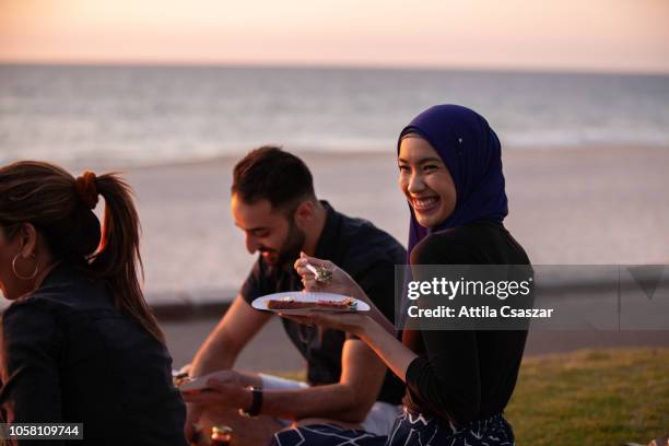 young friends hanging out, enjoying picnic at sunset at beach - muslim woman beach stock-fotos und bilder