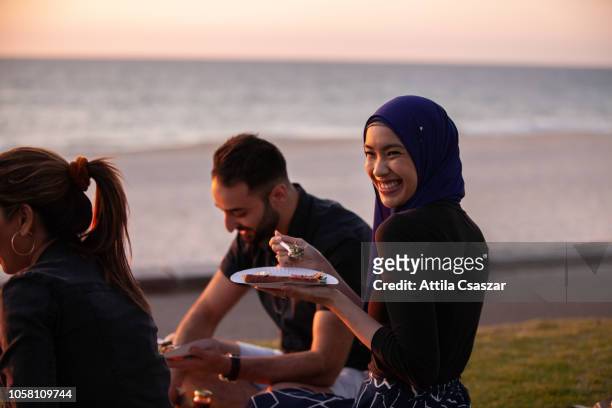 young friends hanging out, enjoying picnic at sunset at beach - muslim woman beach stock pictures, royalty-free photos & images