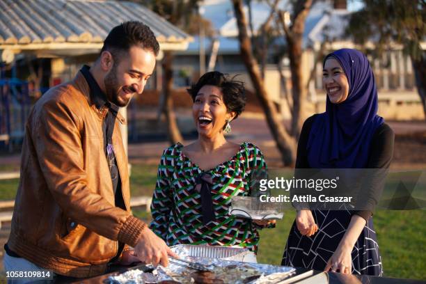cheerful friends enjoying barbecue at beach - muslim woman beach stock-fotos und bilder