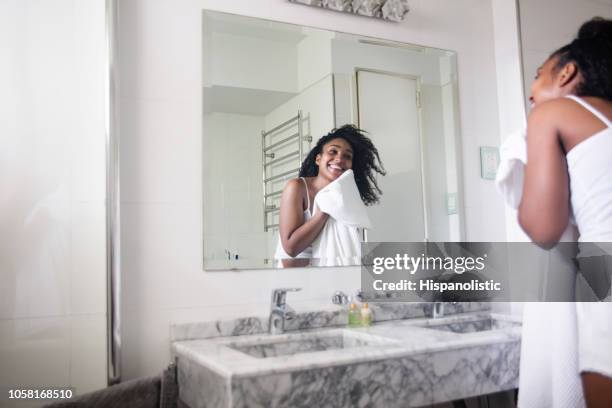 mooie zwarte vrouw haar gezicht met een handdoek drogen terwijl kijken naar zichzelf in de spiegel glimlachen - woman in bathroom stockfoto's en -beelden