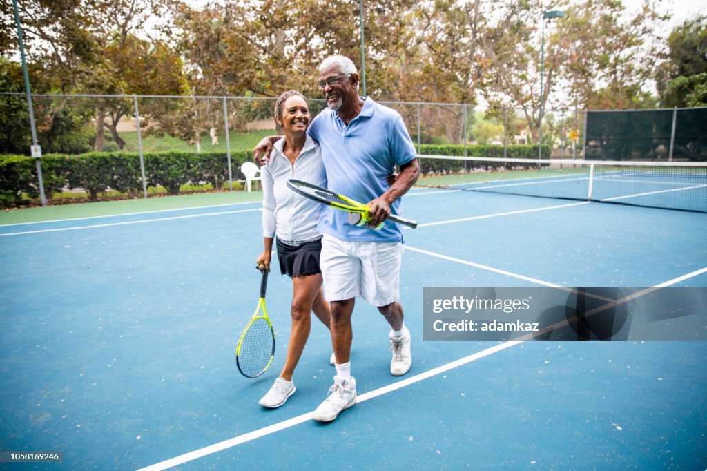 Senior zwart paar lopen uit de tennisbaan