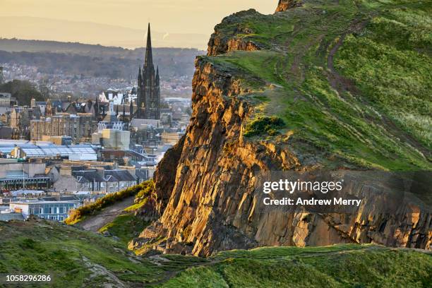 rocky cliffs of salisbury crags in holyrood park with edinburgh city the in background at sunset - holyrood park 個照片及圖片檔