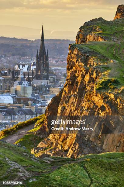 rocky cliffs of salisbury crags in holyrood park with edinburgh city the in background at sunset - edinburgh scotland stock pictures, royalty-free photos & images