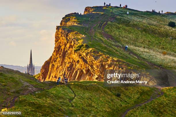 rocky cliffs of salisbury crags illuminated by the sun with church spire, holyrood park, edinburgh - holyrood park 個照片及圖片檔