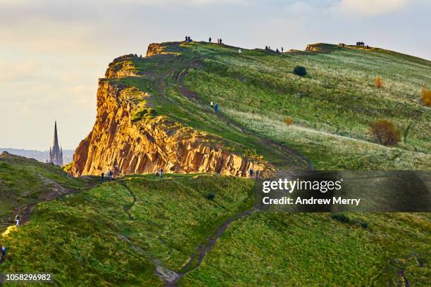 rocky cliffs of salisbury crags illuminated by the sun with church spire, holyrood park, edinburgh - holyrood park stock-fotos und bilder