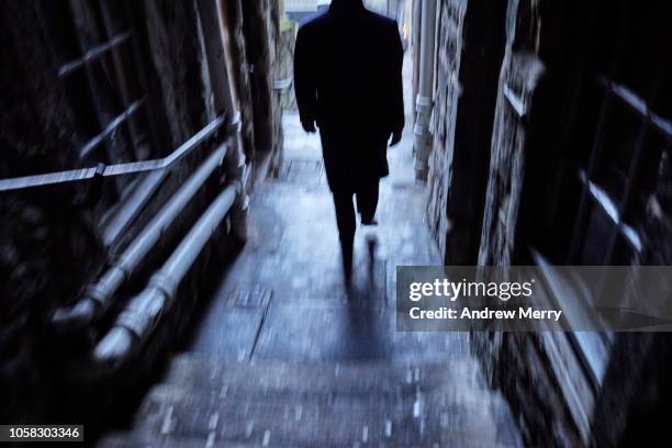 man with black coat walking down a narrow alley, footpath, thoroughfare from the royal mile, edinburgh - フィルム・ノワール風 ストックフォトと画像