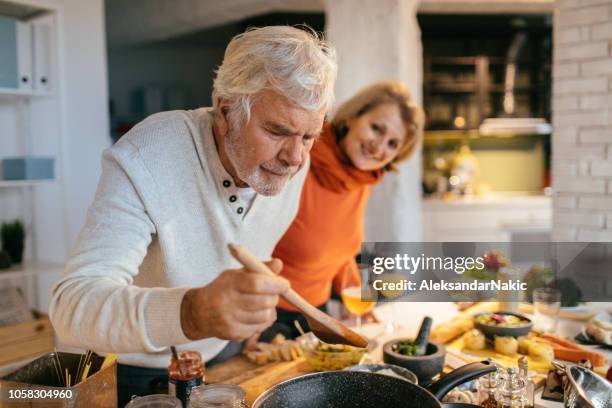 tasting the food they've prepared - healthy older couple stock pictures, royalty-free photos & images