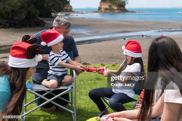 children pulling a christmas cracker at a beach party - new zealand christmas stock pictures, royalty-free photos & images