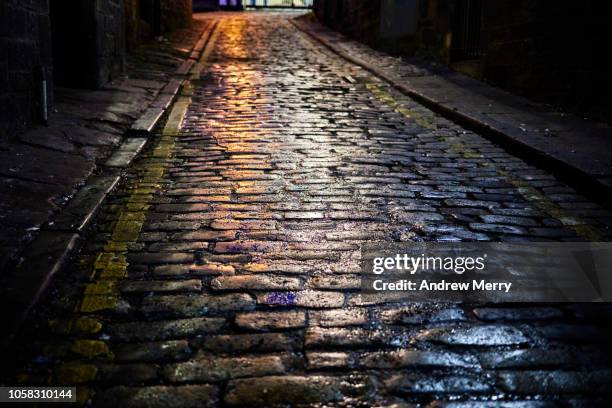 old-fashioned stone paved road at night wet with rain and reflecting street lights, old town, edinburgh - adoquinado fotografías e imágenes de stock