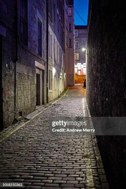 edinburgh old town cobblestone narrow alley, street at night with light at end with dark blue sky - edinburgh rain stock pictures, royalty-free photos & images