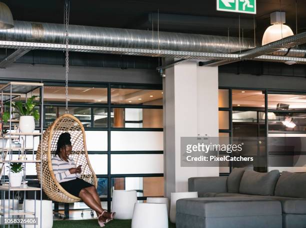 wide shot young businesswoman using her smart phone in communal office area - hanging chair stock pictures, royalty-free photos & images