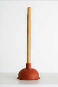 Red plunger with wooden grip against bright white background
