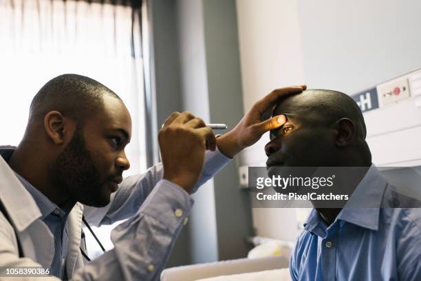 young african male doctor uses with ophthalmoscope to examine patients eye - examination light stock pictures, royalty-free photos & images