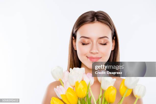International women's day, wellbeing concept. Close up portrait of tender gentle woman with pure flawless face skin smelling aroma of tulips with close eyes isolated on white background