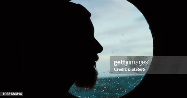 mann am bullaugenfenster eines schiffes, das auf dem meer segelt - bullauge stock-fotos und bilder