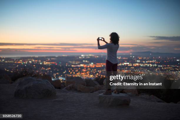 young woman taking a photo of the sunset over the city - city photos fotografías e imágenes de stock