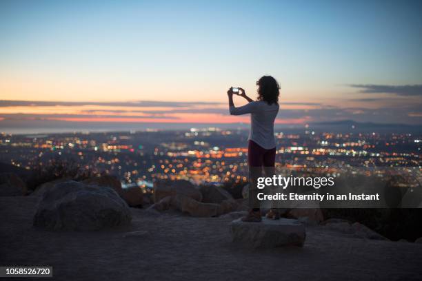 young woman taking a photo of the sunset over the city - city sunset stock pictures, royalty-free photos & images