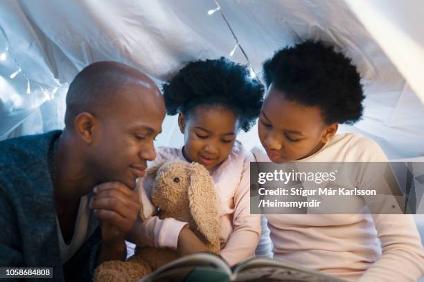 father looking at daughters reading picture book - bedtime story book stock pictures, royalty-free photos & images