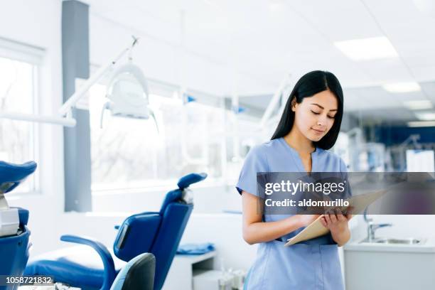 lovely latin nurse standing and writing on clipboard - assistans stock pictures, royalty-free photos & images