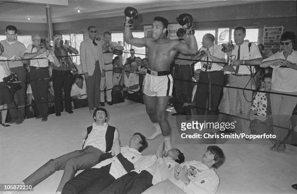 American heavyweight boxer Cassius Clay poses in the ring in mock victory over British pop group The Beatles at the 5th Street Gym in Miami, during...