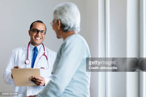 male doctor checking senior female patient and smiling - males stock pictures, royalty-free photos & images