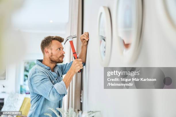 knappe jongeman hameren spijker op witte muur - hamer stockfoto's en -beelden